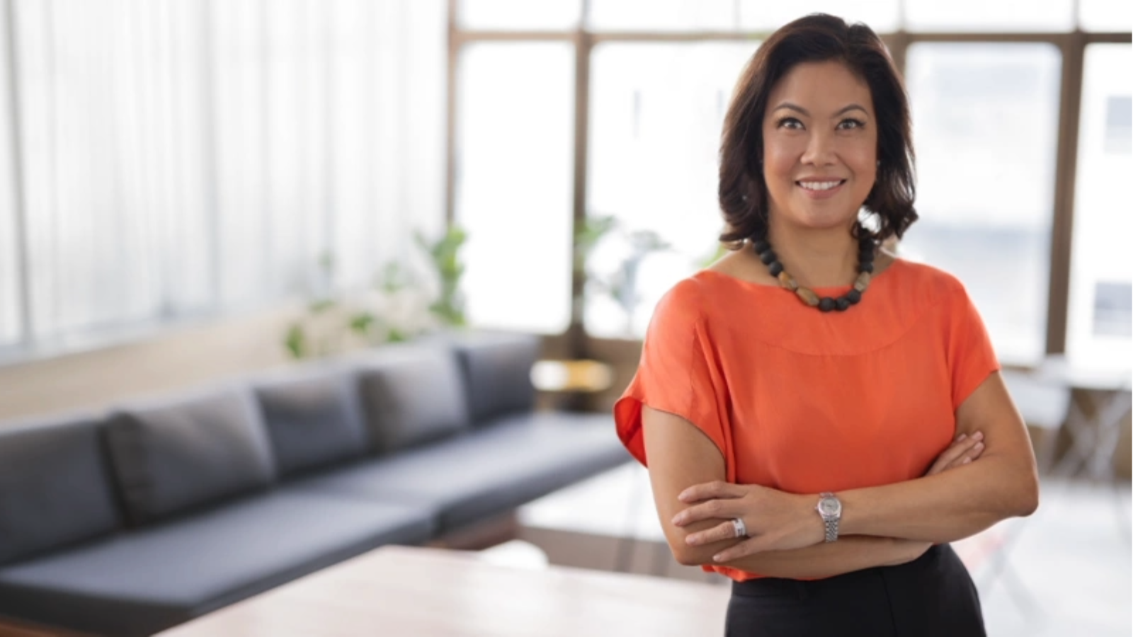Woman with orange top standing with crossed arms
